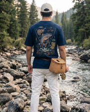 Man wearing Baith The Beast graphic design T-shirt by Toneos, by a river with fishing gear, wearing a blue t-shirt and white pants.